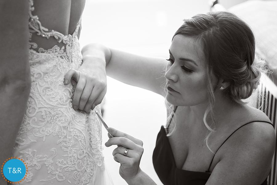 The maid of honor helping the bride button up her dress