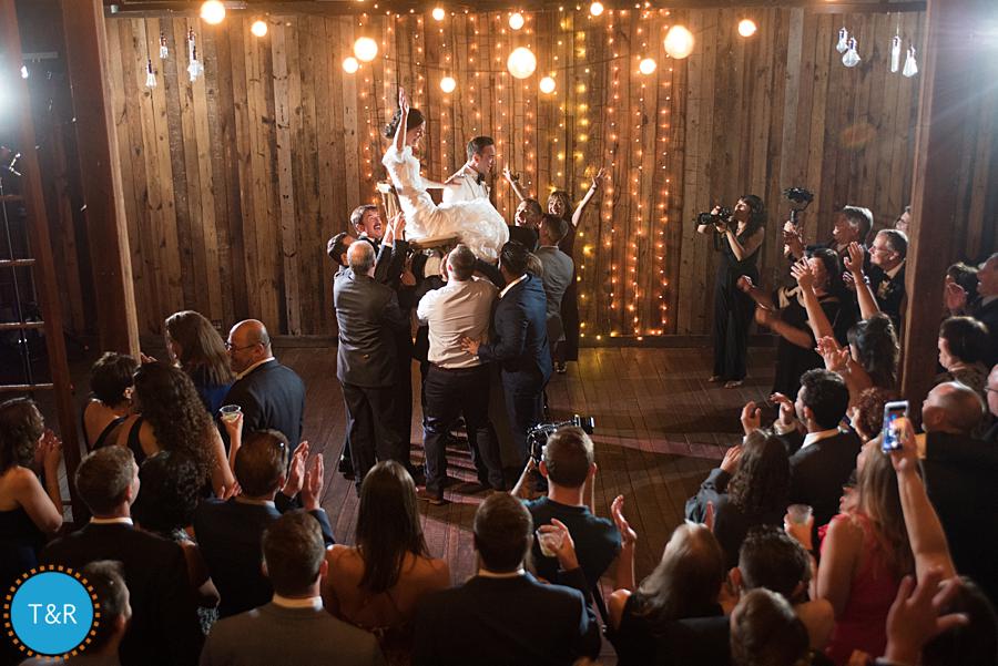 guests lift wedding couple up on chairs and dance