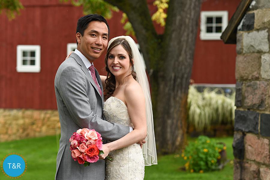 Bride and groom embrace and smile outside the red barn at Zingerman's Cornman Farms in Ann Arbor