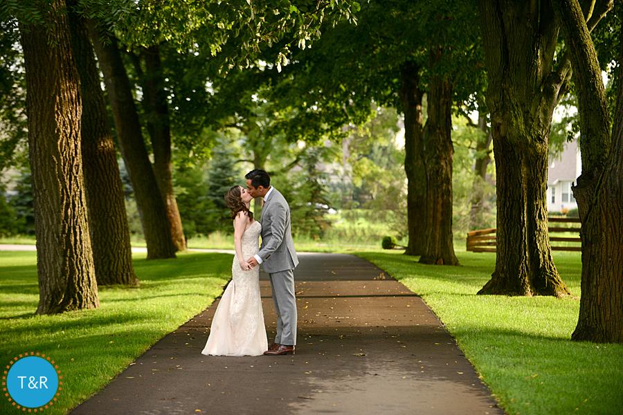 Bride and groom kiss under the trees on the grounds at Zingerman's Cornman Farms Wedding in Ann Arbor