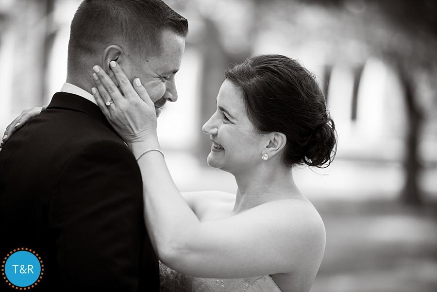 A black and white photo of a bride and groom smiling at each other during wedding photos at University of Michigan's Law Quad in Ann Arbor