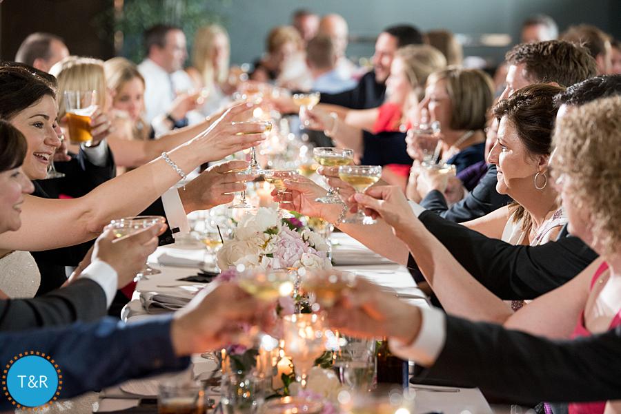 Wedding guests toast by clinking glasses of champagne during the toasts at a Zingerman's Greyline wedding reception