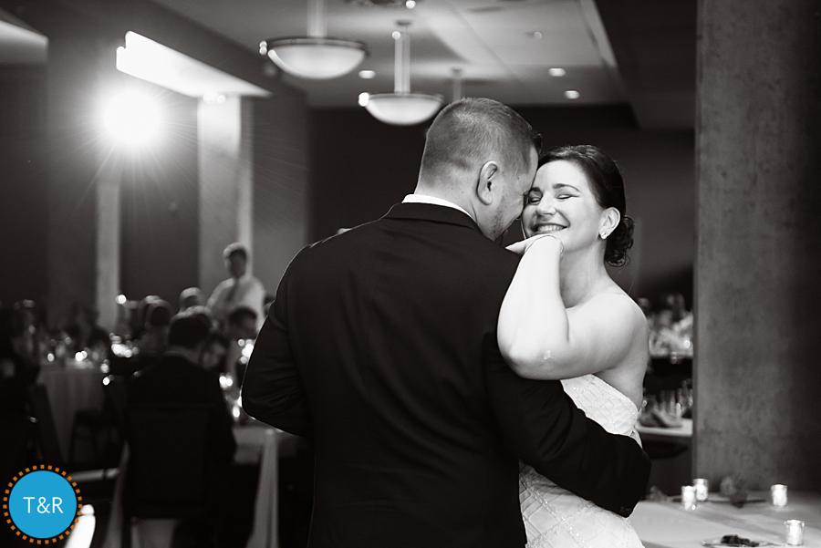 A black and white photo of a bride and groom smiling and dancing during their wedding reception at Zingerman's Greyline in Ann Arbor