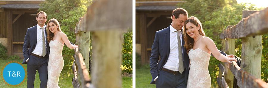 Bride and groom laugh and embrace near a rustic fence outside the barn at their Frutig Farms Misty Farm wedding
